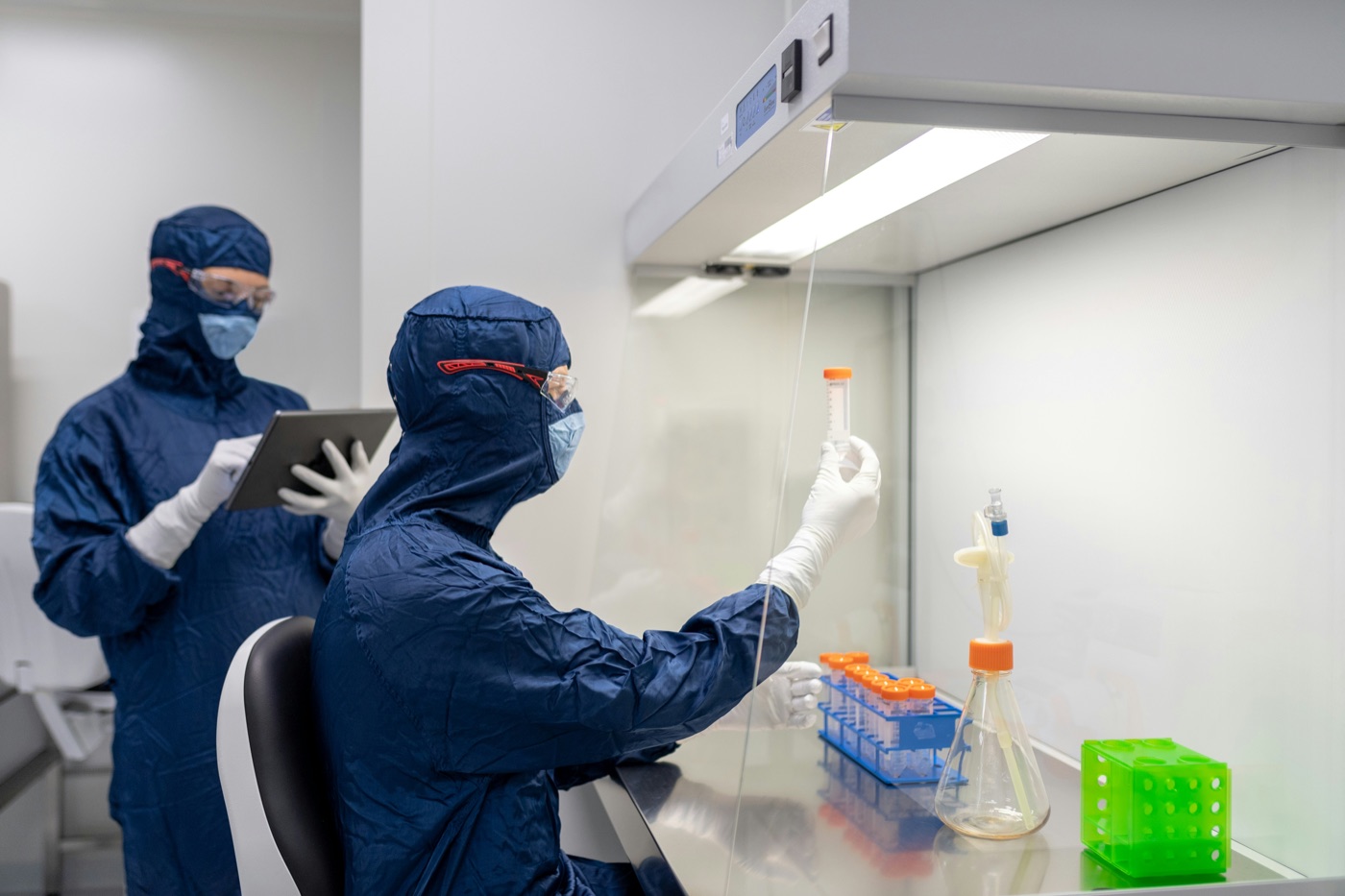 Bulk Labs technicians in cleanroom suits testing product samples under a laminar flow hood